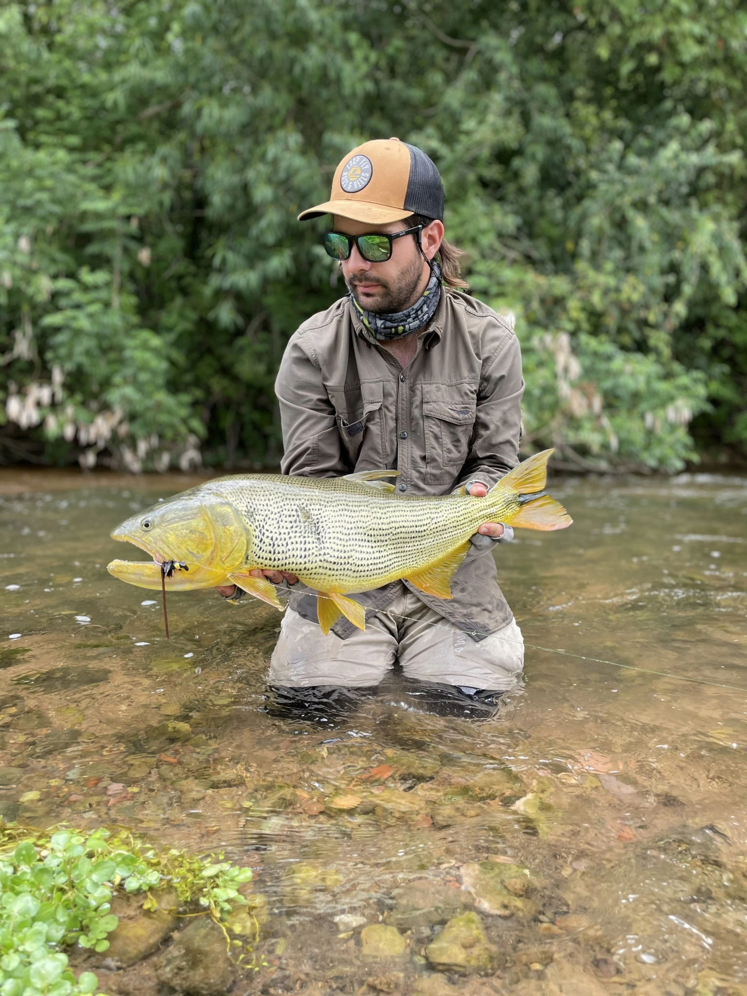 Un pescador muestra su captura junto al agua.